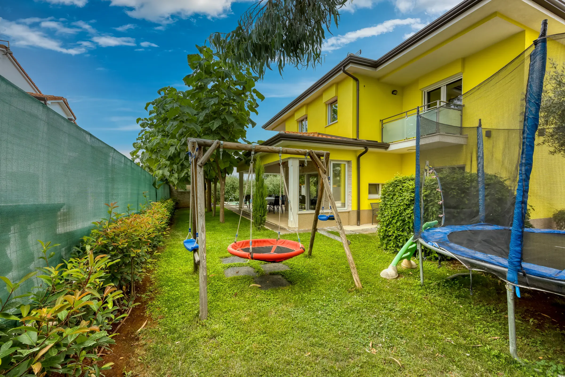 Play area with trampoline, swings and nest swing next to the villa